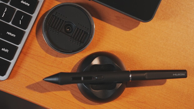 Digital pen resting on circular black stand next to laptop keyboard on wooden desk.