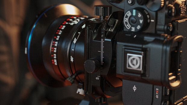 Professional cinema camera with red macro lens and focus wheel mounted on adjustable support rig.