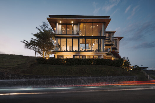 Modern multi-story residential building with illuminated interiors photographed at dusk, long exposure light trails visible on road below.