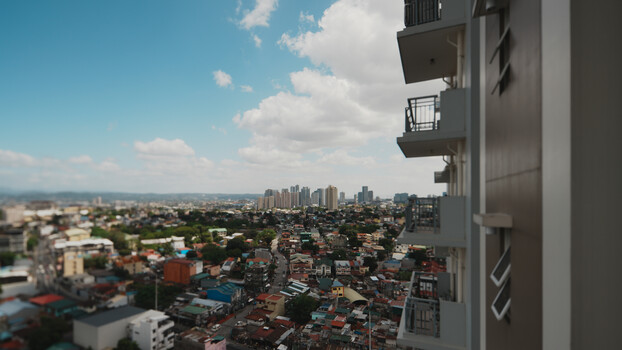 Aerial view from high-rise balcony overlooking dense urban cityscape with distant skyline and mountains.