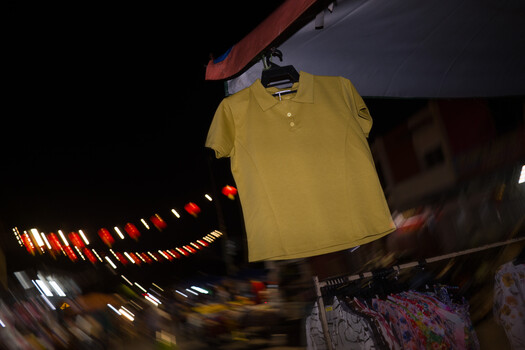 Yellow polo shirt hanging from a display rod with blurred retail storefront and warm lighting in background.