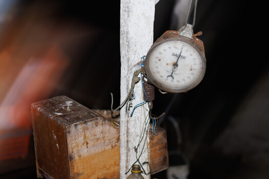 Vintage hanging scale with weathered wooden base mounted on a white post.