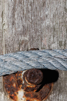 Weathered rope looped through a rusted metal ring mounted on distressed wooden surface.