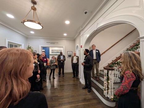 Group of people gathered in an elegant hallway with arched doorway and holiday decorations.