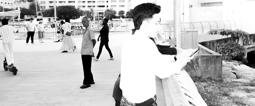 Black and white photograph of people in an outdoor public space with modern buildings in the background.