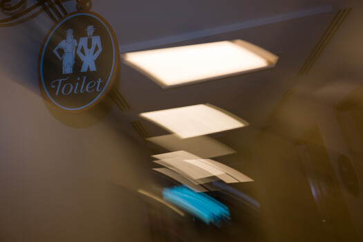 Toilet sign with motion blur of person walking down hallway with recessed ceiling lights.