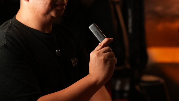 Person holding a microphone against a dark background with warm orange stage lighting.