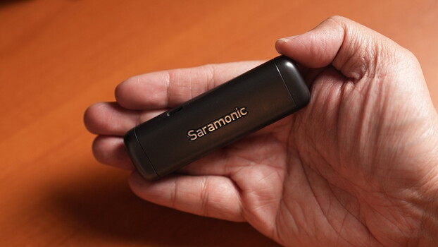 Hand holding a black Saramonic wireless microphone against an orange background.