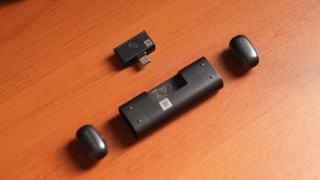 Three black wireless audio devices arranged on an orange wooden surface.