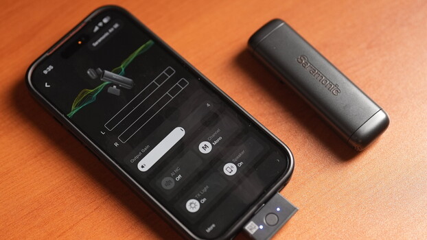 Smartphone displaying audio editing interface with waveform and control sliders, next to a cylindrical external audio device on orange background.