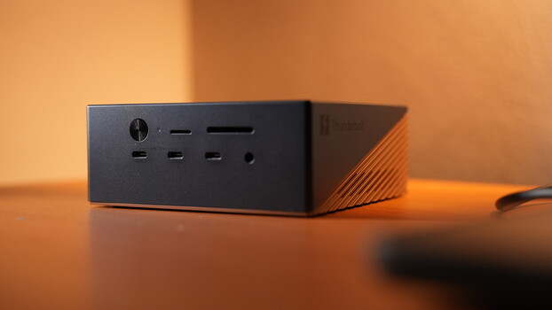 Dark compact desktop computer with ribbed side panel on wooden surface under warm orange lighting.