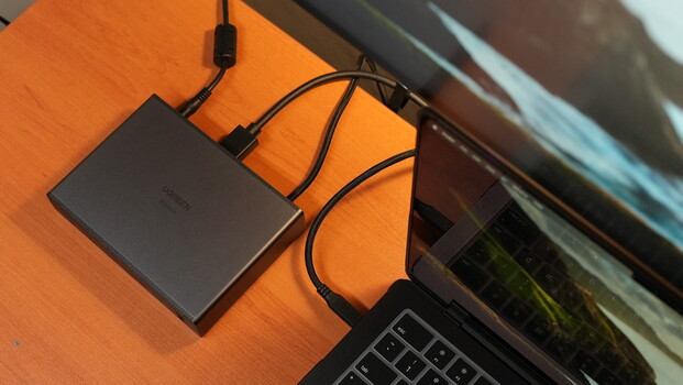 External hard drive connected to laptop via USB cable on wooden desk surface.