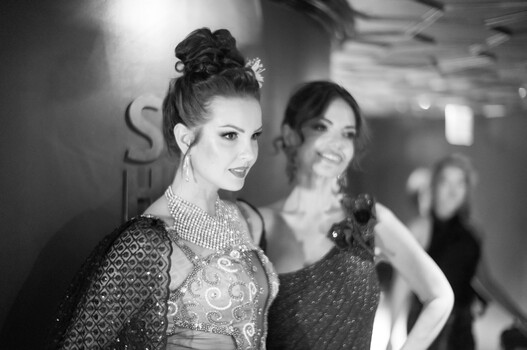 Two women at an event in black and white, one facing camera with styled hair and jewelry.
