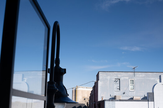 View through a truck's side mirror showing urban buildings and clear blue sky.