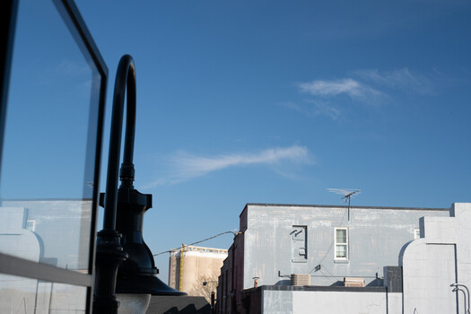 View from inside a vehicle showing the side mirror and industrial buildings under blue sky.