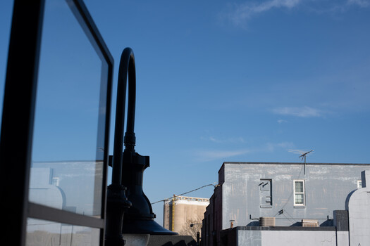 View through a vehicle's side mirror and window toward urban buildings under clear blue sky.