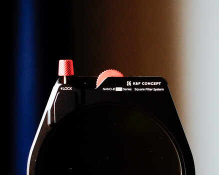 Close-up of a camera's top plate showing shutter button, mode dial, and control labels against a gradient blue-to-white background.