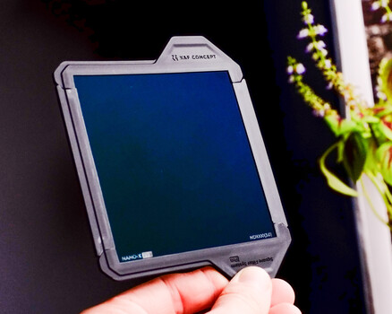 Hand holding a portable monitor or display device with blue screen against dark background.