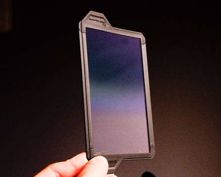 Hand holding a smartphone displaying a gradient sky transitioning from deep purple to pink and white.