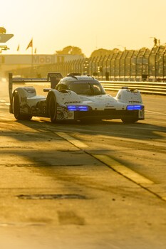 Race car with blue headlights navigating a wet racetrack at golden hour.