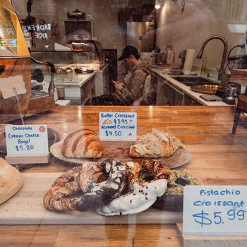 Bakery display case with croissants, pastries, and a pistachio croissant with price signage.