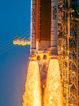 Rocket launch at twilight with massive flame exhaust illuminating the sky and launch structure.
