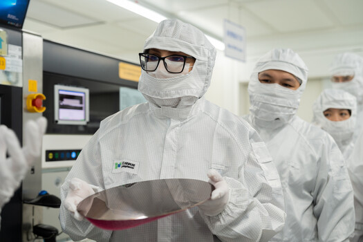 Cleanroom technician in full protective gear holding a large semiconductor wafer.