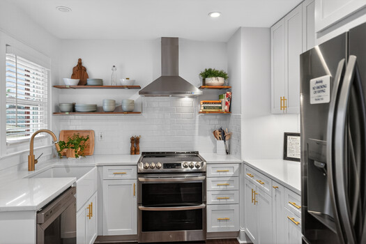 Modern kitchen with white cabinetry, stainless steel appliances, and open shelving displaying dishware and plants.