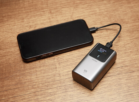 Portable power bank with digital display connected to smartphone via USB cable on wooden surface.
