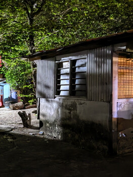 Small corrugated metal structure with ivy-covered walls and horizontal louvered window.