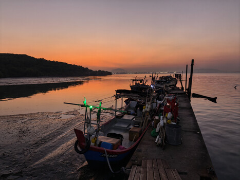 Wooden dock lined with fishing boats at twilight, golden sky reflecting on calm water.