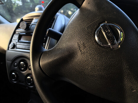 Close-up of a black leather steering wheel with chrome horn pad emblem in a vehicle interior.
