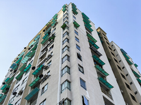 Tall residential building photographed from ground level with upward-looking perspective against clear sky.