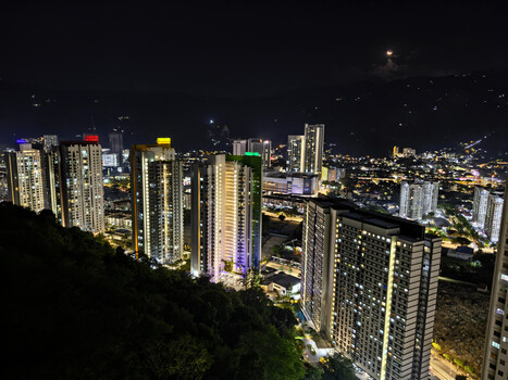Nighttime cityscape with illuminated high-rise residential towers and distant city lights in the background.