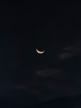 Crescent moon against dark night sky with silhouetted clouds.