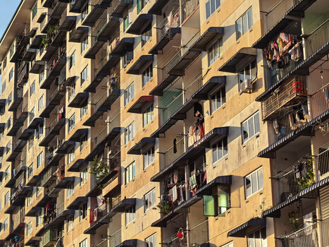 Densely packed residential apartment building facade with weathered yellow and brown tones, multiple balconies, and varied window arrangements.