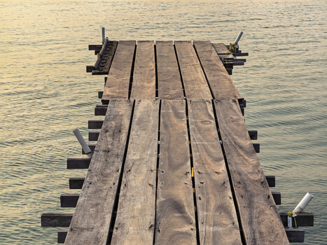 Wooden pier extending into calm water, photographed from above at golden hour.