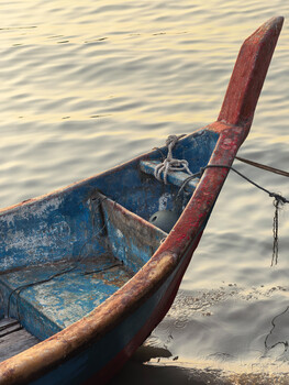 Weathered blue and red wooden boat moored in shallow water with anchor visible.