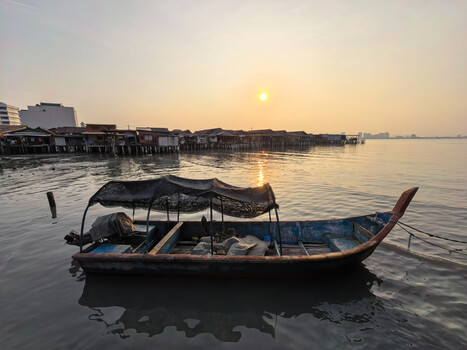 Traditional wooden boat with canopy floating on calm water at sunrise.