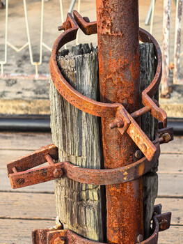 Rusted metal bands wrapped around a weathered wooden post with visible patina and decay.