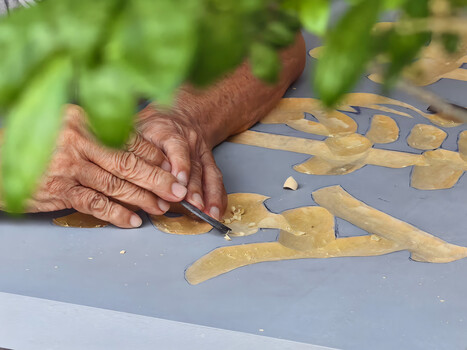 Hands working on detailed gold leaf cutouts positioned on a gray surface.