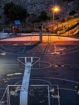 Empty basketball court at dusk illuminated by a single streetlight beneath a starry sky.