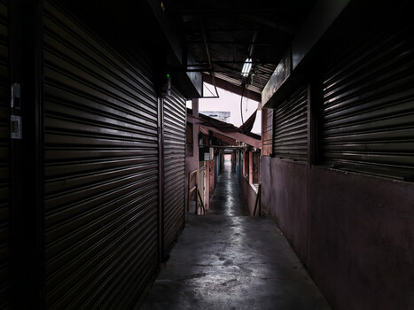 Narrow alleyway between metal roller shutters with wet pavement and bright opening ahead.