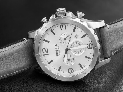Fossil chronograph watch with white dial and gray leather strap on dark surface.