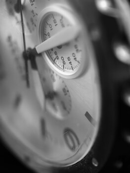 Close-up black and white photograph of analog gauge faces with overlapping needles and numbered dials.