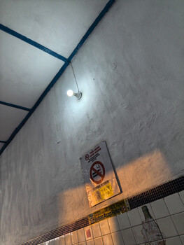 Concrete ceiling with exposed blue structural beams and a single recessed light fixture casting bright illumination downward.