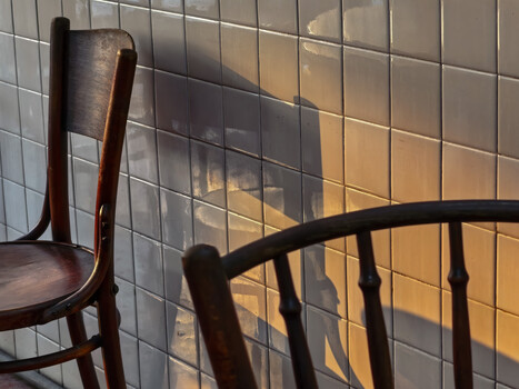 Wooden chair silhouettes cast on a light-colored tiled wall by warm afternoon sunlight.