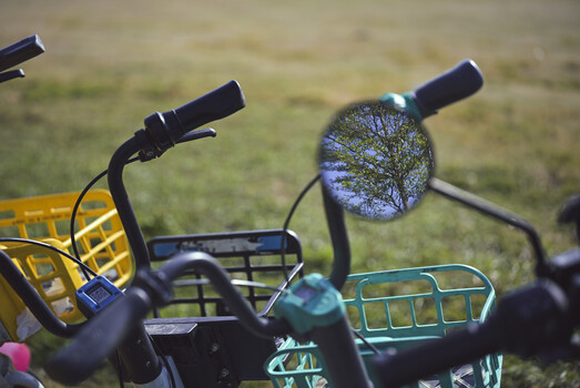 Close-up of bicycle handlebars and mirrors with blurred green background in shallow focus.