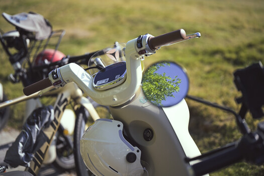 Close-up of a vintage scooter's chrome handlebars and headlight mirror reflecting a tree and blue sky.