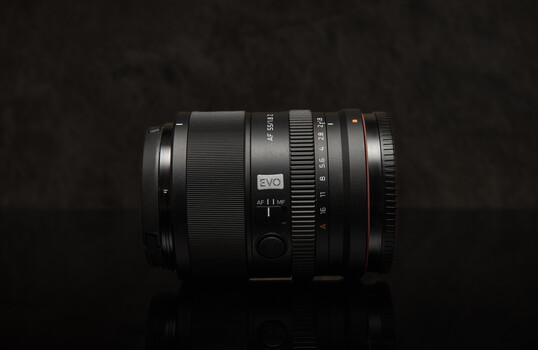 A collection of camera lenses arranged on a dark reflective surface.